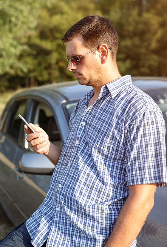 Un homme adossé à sa voiture consulte son téléphone portable